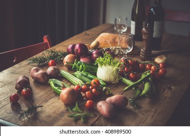 Different Fresh Farm Vegetables On Wooden Table. Wine Bottles And Bread On Background. Autumn Harvest And Healthy Organic Food Concept. Toned Picture
