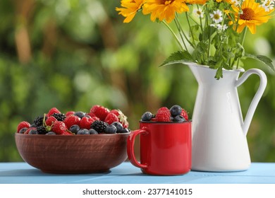 Different fresh ripe berries and beautiful flowers on light blue table outdoors - Shutterstock ID 2377141015