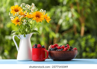 Different fresh ripe berries and beautiful flowers on light blue table outdoors - Shutterstock ID 2377141049