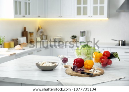 Different fresh vegetables and mushrooms on white table in modern kitchen. Space for text