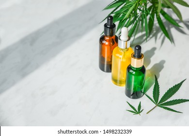 Different glass bottles with CBD OIL, THC tincture and cannabis leaves on yellow background. Flat lay