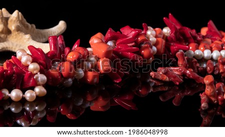 Different glittering red coral and white mother of pearl necklaces on a black background. Luxurious natural jewelry close up. 
