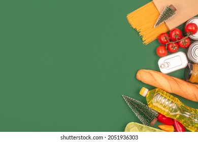 Different Groceries, Christmas Food Donations On Green Background With Copy Space - Pasta, Vegatables, Canned Food, Baguette, Cooking Oil, Tomatoes. Food Bank, Food Delivery Concept. Selective Focus