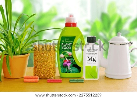 Different indoor fertilizers: fertiliser sticks or spikes, granules, liquid and speciality plant food in bottles, against a green plants background.