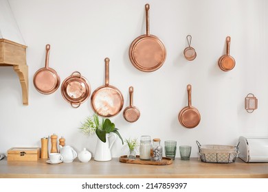 Different kind of cookware and ceramic plates on tabletop wooden kitchen. Set of copper saucepans, pans, pots and ladle hanging in kitchen. Hanging kitchen utensil on wall. kitchen interior decor
 - Shutterstock ID 2147859397