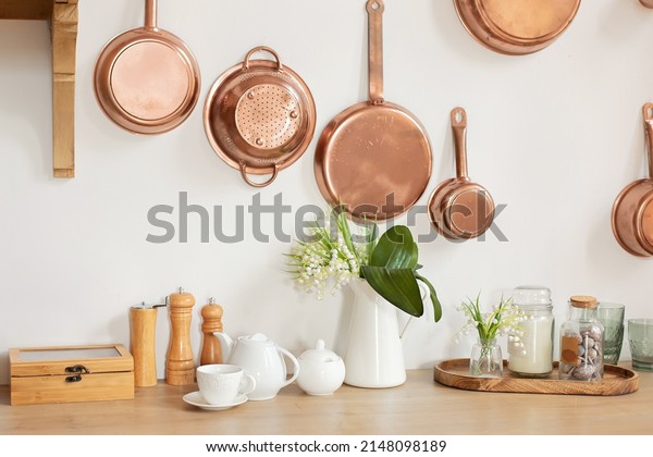 Different kind of cookware and ceramic plates on\
tabletop wooden kitchen. Set of copper saucepans, pans, pots and\
ladle hanging in kitchen. Hanging kitchen utensil on wall. kitchen\
interior decor\
