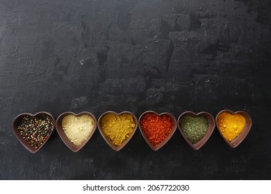 Different kind of spices on a black stone. Oriental spices in in heart shaped bowl, red peppers, curry powder, cinnamon powder, mint powder, colorful peppers. Flat lay, top view. - Powered by Shutterstock