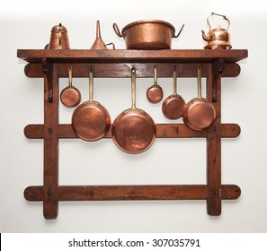 Different kind of vintage copper cookware, pans, coffee pot and funnell hung on wooden shelf in kitchen