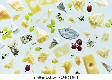 Different kinds of cheeses Blue cheese pieces, Parmesan, camembert, Tete de Moine, Gruyere and grapes flying in the air with crumbs isolated on white background. Cheeses plate menu.