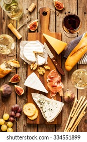 Different Kinds Of Cheeses, Wine, Baguette, Fruits And Snacks On Rustic Wooden Table From Above. French Tasting Party Or Feast Scenery.