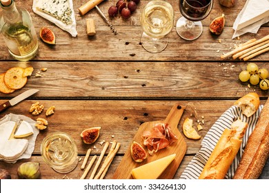 Different Kinds Of Cheeses, Wine, Baguettes, Fruits And Snacks On Rustic Wooden Table From Above. French Tasting Party Or Feast Scenery. Layout With Free Text Space. 