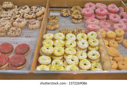 Different kinds of colourful ring dougnuts with glaze, sprinkles and fillings exposed in a bakery shop