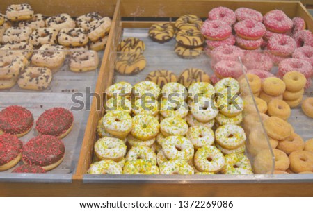 Different kinds of colourful ring dougnuts with glaze, sprinkles and fillings exposed in a bakery shop