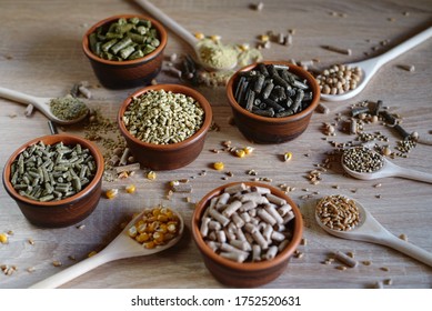 Different kinds of pelleted compound feed in bowls and spoons on wood table, copy space
