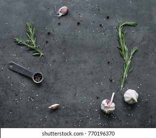 Different Kinds Of Spices: Rosemary, Salt, Pepper And Garlic On The Dark Slate Or Stone Background With Metal Measuring Cup. Food Flatlay Top View With Copy Space For Text