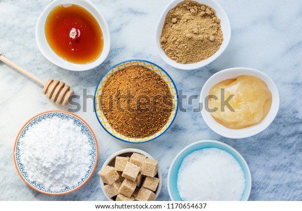 Different Kinds of Sugar and Sweeteners in the\
Bowls, such as coconut, pure cane, icing, maple syrup, dark brown\
soft sugar, honey, demerara\
cubes