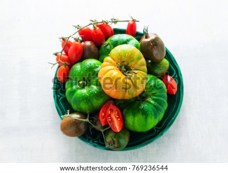 different kinds of tomatoes on a plate on a white stone table. fresh ripe ingredients for a healthy diet. proper nutrition
