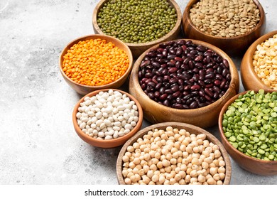 Different legumes. Mung beans, red and white beans, lentils, peas and chickpeas in wooden bowls on the light grey kitchen table closeup. Vegetarian food