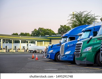 Different Make And Models Big Rigs Semi Trucks With Semi Trailers Standing In Row On Truck Stop Parking Lot For Rest And Comply With The Movement According To The Schedule For Successful Delivery