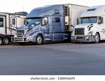 Different Make And Models Big Rigs Semi Trucks With Semi Trailers Standing In Row On Truck Stop Parking Lot For Rest And Comply With The Movement According To The Schedule For Successful Delivery