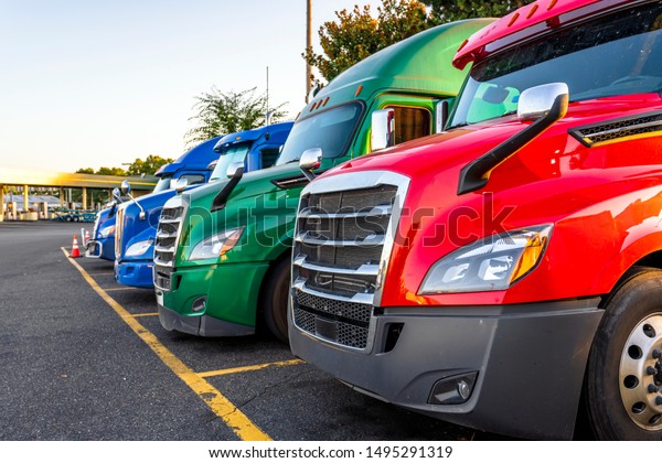 Different make and models big rigs semi trucks\
with semi trailers standing in row on truck stop parking lot for\
rest and comply with the movement according to the schedule for\
successful delivery