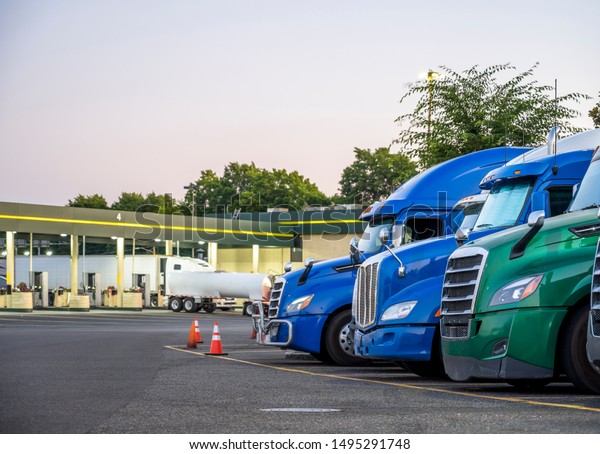 Different make and models big rigs semi trucks\
with semi trailers standing in row on truck stop parking lot for\
rest and comply with the movement according to the schedule for\
successful delivery