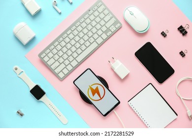 Different modern gadgets and mobile phone charging with wireless pad on color background