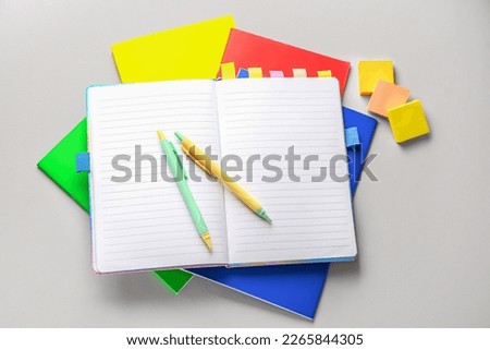 Different notebooks, sticky notes and pens on light background