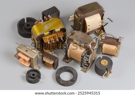 Different old compact mains shell type transformers and transformer with pot type ferrite core for use in various devices power supplies and their parts on a gray surface