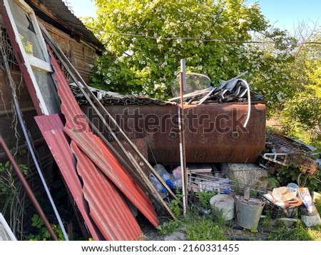 Different old stuff stored in the garden. Metal pieces, wooden window frames, rusty tank and old buckets in the garden