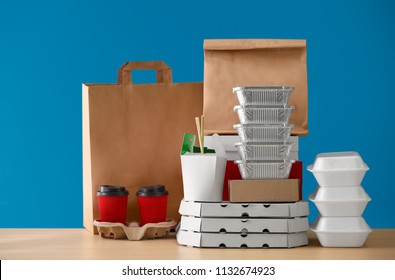 Different packages and carton cups on table against color background. Food delivery service