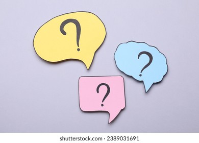 Different paper speech bubbles with question marks on light grey background, flat lay