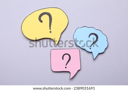 Different paper speech bubbles with question marks on light grey background, flat lay