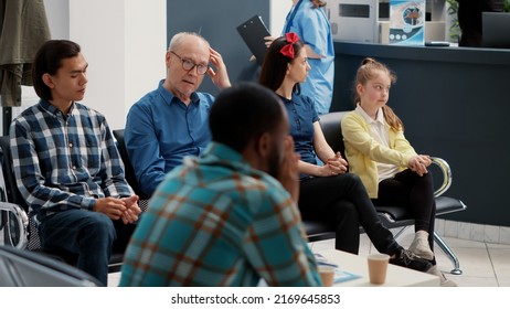 Different people waiting in row at hospital reception lobby to be called in office at checkup visit examination with specialist. Waiting room area for medical consultation at busy clinic.