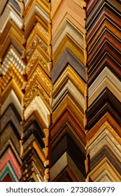 Different picture frames are stacked in a zigzag pattern on display in an art shop. The frames vary in color and design, showcasing a range of materials and styles.