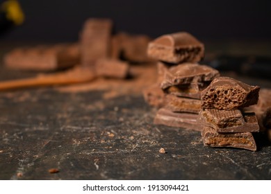 Different Pieces Of Dark Chocolate And Cocoa Powder On A Dark Surface.