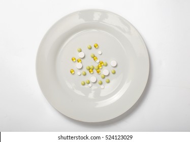 Different pills on a white plate on a white background, top view