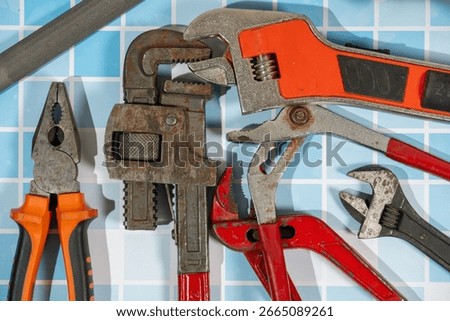 Different plumbing tools lying on blue tiles, ready for a home repair job