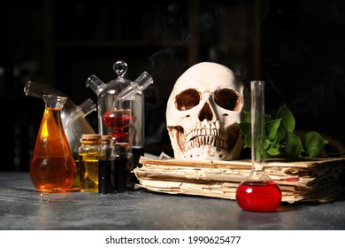 Different potions, old book and human skull on alchemist's table