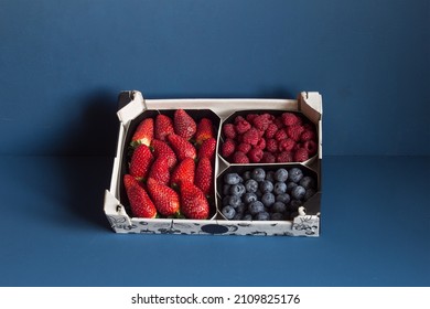 Different red berries in a patterned cardboard basket and blue textured background. Groceries and fruit.