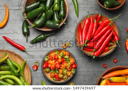 Different ripe hot chili peppers on grey table, flat lay