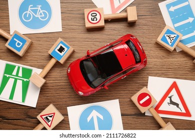 Different road signs and toy car on wooden table, flat lay. Driving school