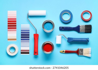 Different rollers with brushes, cans of paints, palette samples and adhesive tape rolls on blue background