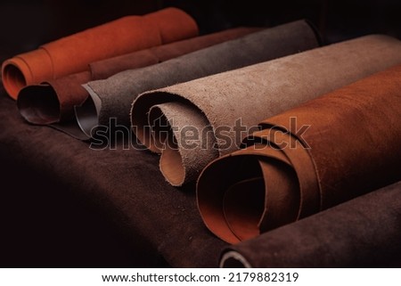 Different rolls of natural color leather on rack in workshop. Materials for DIY handmade craft.