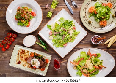 Different Salads On Wooden Table, Top View. Vegetable Salad, Salad With Smoked Salmon, Baked Meat With Vegetables. Food Background, Top View