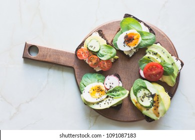 Different sandwiches with vegetables, eggs, avocado, tomato, rye bread on light marble table. View from above. Appetizer for party. Flat lay.