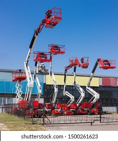Different self propelled articulated boom lifts and one scissor lift red with white colors on a background of industrial building and clear sky - Shutterstock ID 1500261623