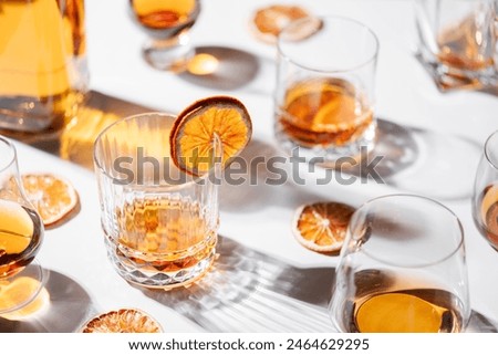 Different shape glasses with whiskey on white table. Dried oranges decoration. Alcohol concept