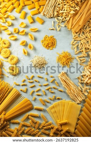 Different shapes of pasta are creating a frame on a gray background, showcasing italian culinary tradition