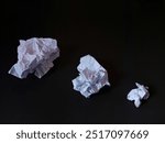 Different size crumpled white paper ball against a dark background. The image highlights the textures and folds of the paper, symbolizing waste, mistakes, or recycling